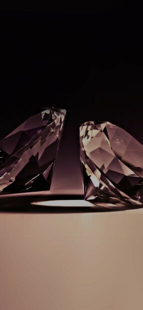 Two clear gemstone crystals reflecting light on a dark surface with sharp edges