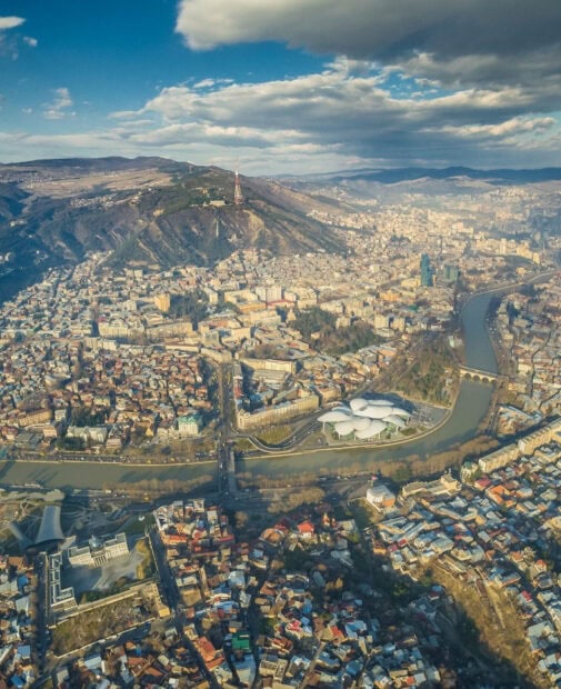 Aerial view of Georgia cityscape with mountains river and modern architecture against blue sky