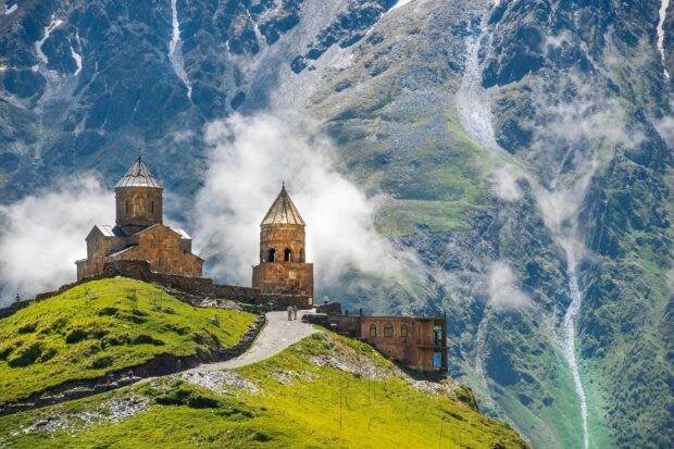 Ancient Georgia church on green hill with mountains in background