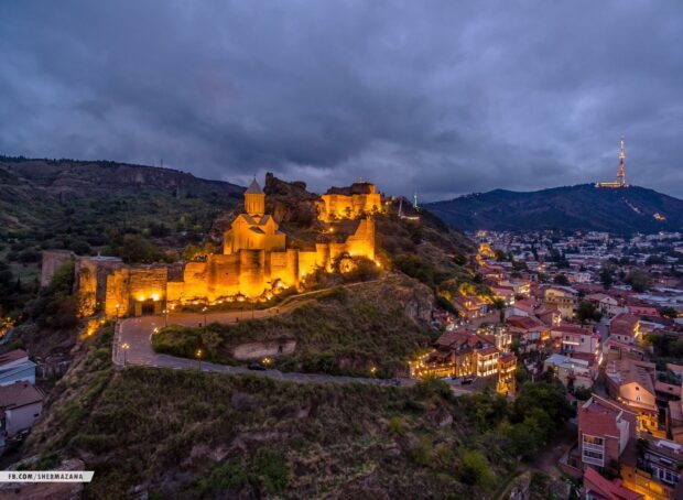 Ancient Georgia fortress illuminated at dusk on a hill overlooking the city