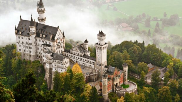 A stunning view of a historic castle in Germany surrounded by lush green forests and mist