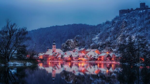 Snow covered village in Germany reflected on a calm river during winter night