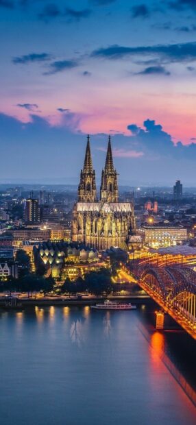 Cologne Cathedral in Germany city skyline at sunset with river and illuminated bridge