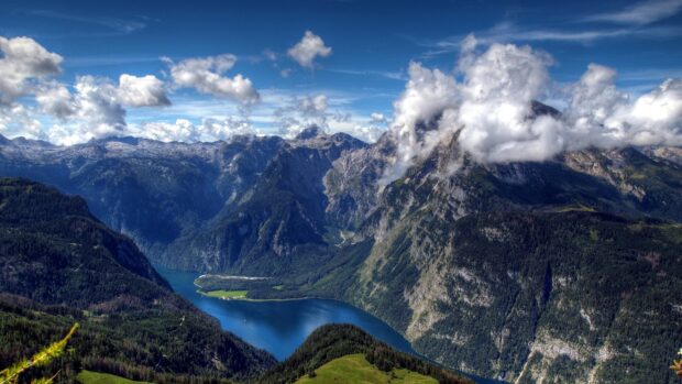 A scenic view of Germany mountains and river under a bright blue sky with clouds