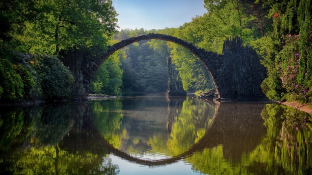 Rakotz Bridge in a forest in Germany reflected on calm water surrounded by lush green trees