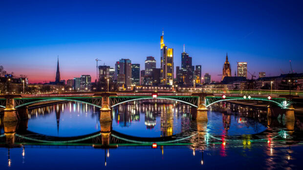 The cityscape of Germany with modern skyscrapers and a bridge reflecting on the water at sunset