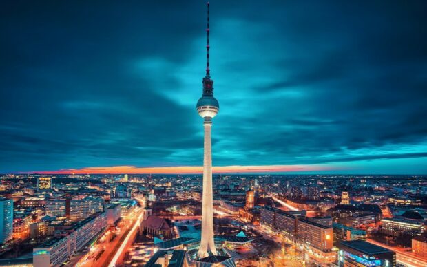 The Berlin TV tower stands tall over the cityscape of Germany at dusk with vibrant city lights
