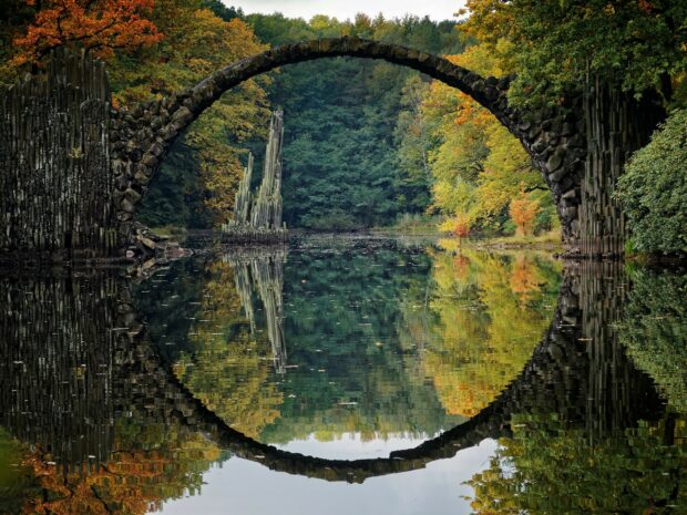 Ancient stone circle and lush forest in Germany reflecting on calm water with autumn colors