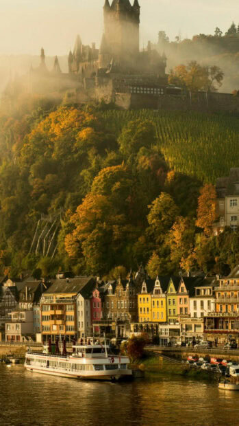 Historic castle and colorful houses along the river in Germany with lush autumn foliage