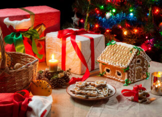 A festive gingerbread house surrounded by decorated Christmas gifts and cookies