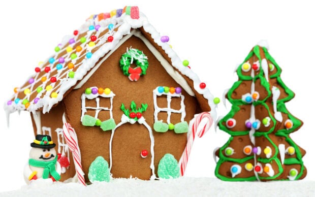 A gingerbread house decorated with colorful candies and icing surrounded by a snowman and gingerbread trees