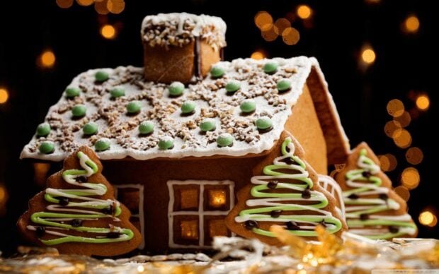 A gingerbread house decorated with icing and candies surrounded by Christmas tree cookies