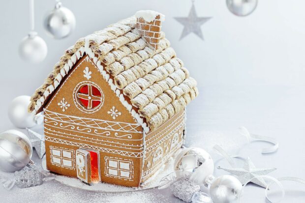 A gingerbread house decorated with icing and surrounded by silver Christmas ornaments