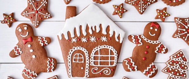 A gingerbread house decorated with icing surrounded by gingerbread men and stars on a wooden surface