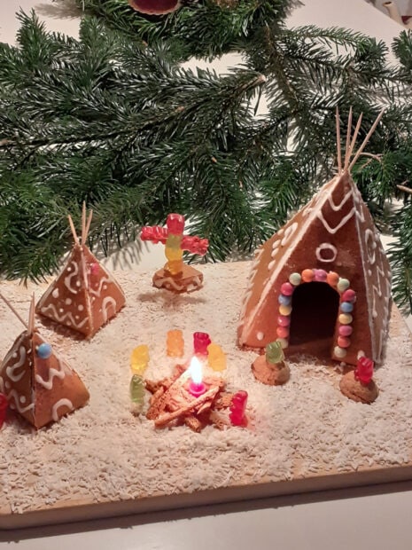 A gingerbread house with decorated pyramids and gummy bears around a lit candle campfire