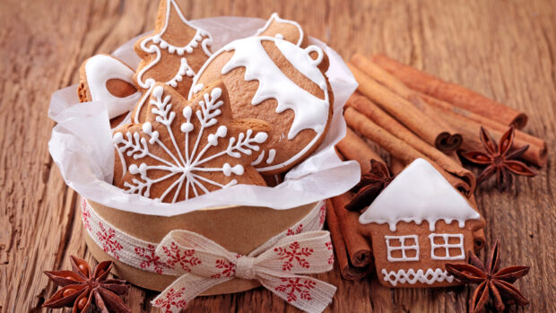 A gingerbread house surrounded by cinnamon sticks and star anise on a wooden surface