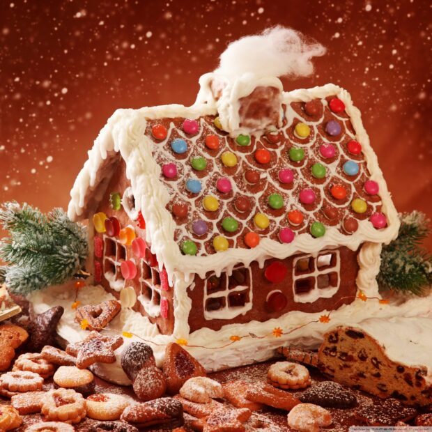 A detailed gingerbread house decorated with colorful candies and white icing surrounded by Christmas cookies