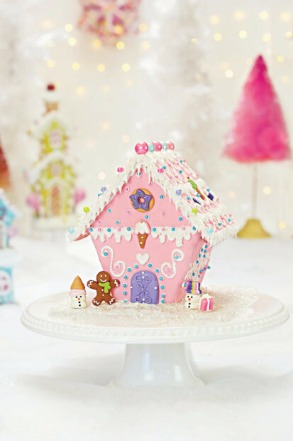 Pink gingerbread house decorated with icing and candies surrounded by festive snowman figures