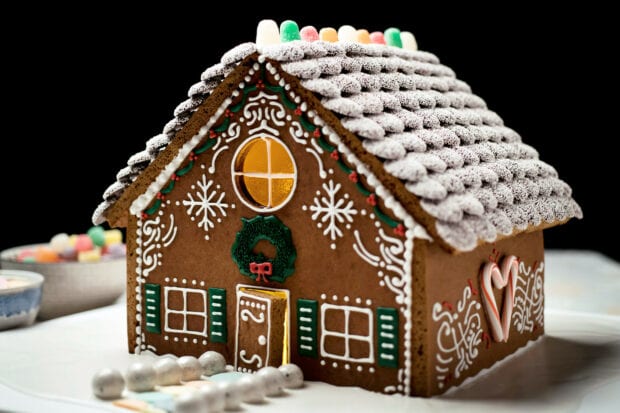 A detailed gingerbread house decorated with icing and candy on a white plate
