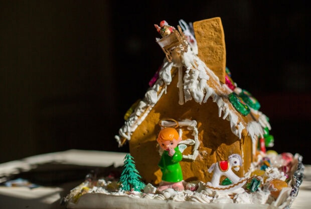 A gingerbread house decorated with an angel figurine and festive ornaments on a table