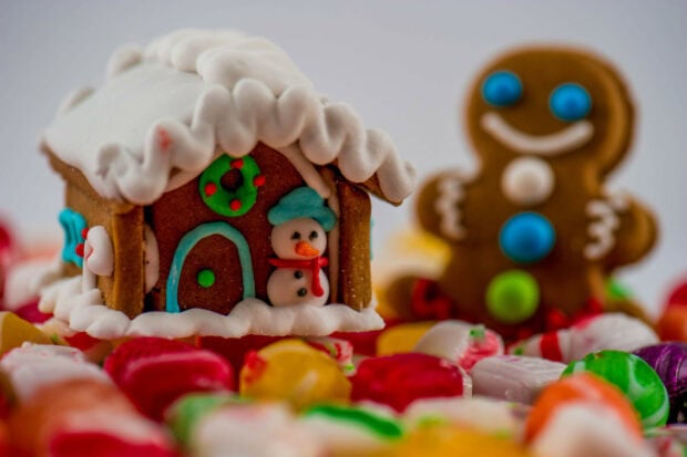 A gingerbread house decorated with white icing and a small snowman surrounded by colorful candies
