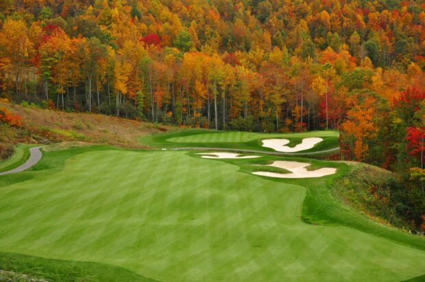 A golf course surrounded by colorful autumn trees with green fairways and sand bunkers