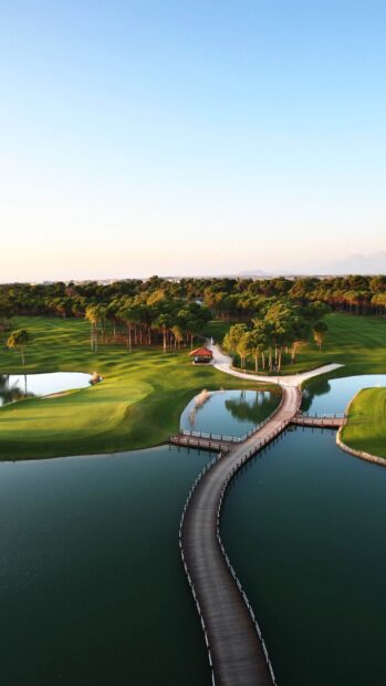 A golf course with a wooden bridge over water surrounded by green trees and grass on a clear day