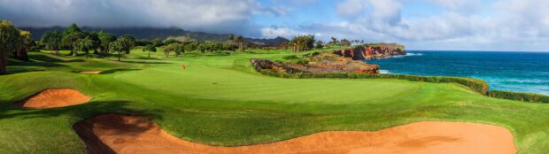 A golf course with lush green grass and sand bunkers near the ocean under a cloudy sky