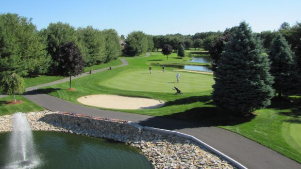 Golf course with players putting on green surrounded by trees and water fountain