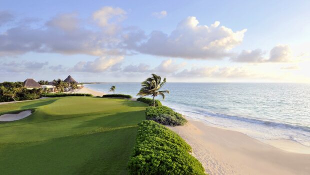 A golf course near the beach with green grass and palm trees under a cloudy sky