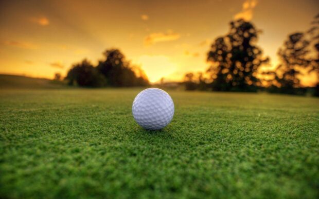 Golf ball on the green grass of a golf course at sunset with trees in the background