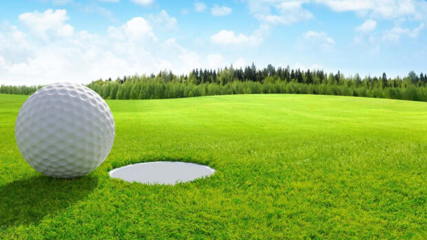 A golf ball resting near the hole on a golf course surrounded by green grass and trees