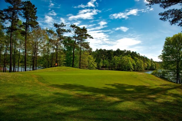 A golf course surrounded by trees and a lake under a partly cloudy sky