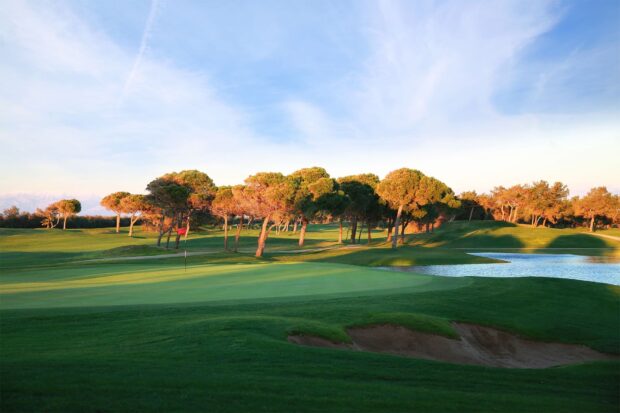 A golf course surrounded by trees and a water hazard on a clear sunny day