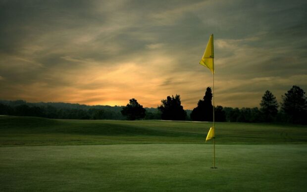 A golf course with a flag on the green during a beautiful sunset golf course