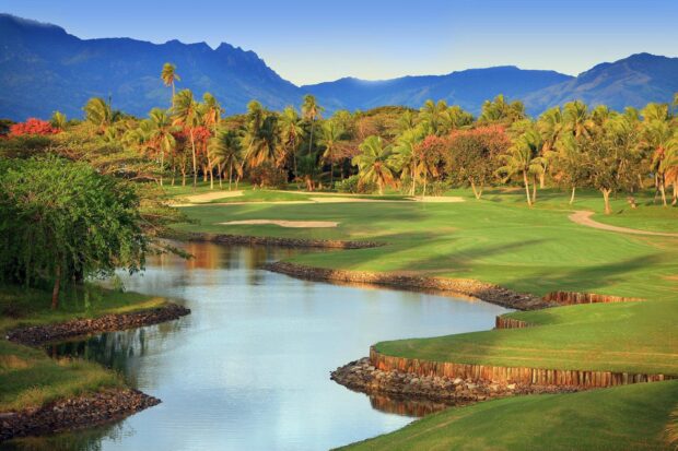 A beautiful golf course featuring lush greenery and water near tropical trees and mountains