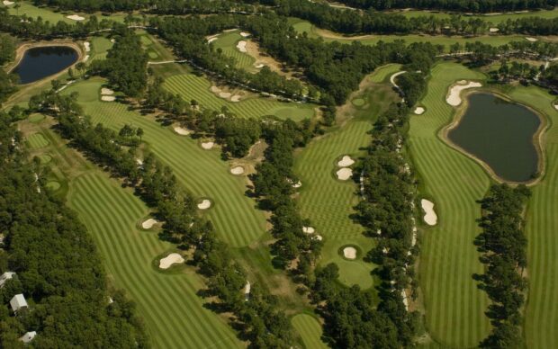 A golf course with striped green fairways surrounded by trees and sand bunkers