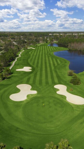 A golf course with green fairways and sand bunkers under a partly cloudy sky