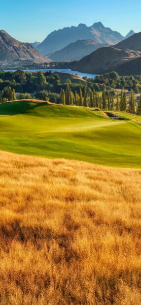 Golden dry grass surrounds the lush green golf course on a mountain landscape