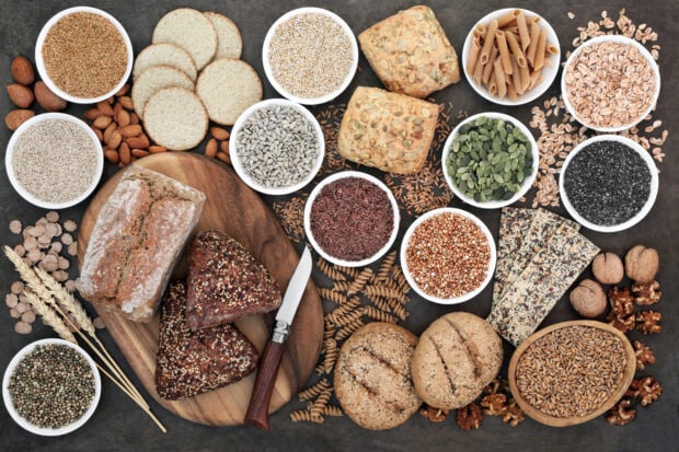 A variety of grains displayed with bread rolls and seeds arranged on a wooden board and bowls