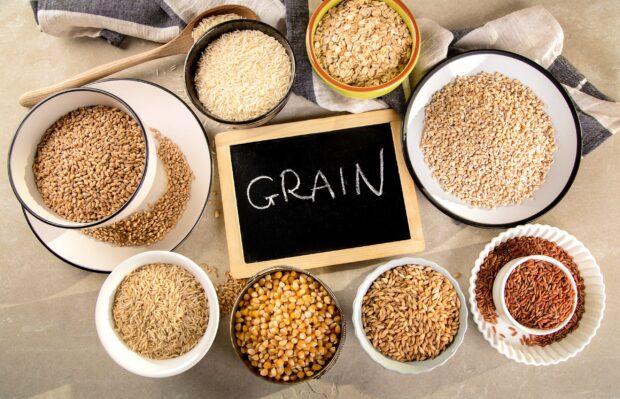Various grains displayed in bowls surrounding a chalkboard with the word grain written on it
