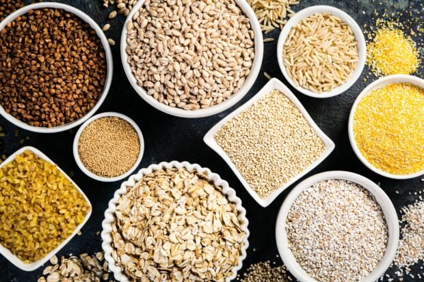 Various grains displayed in white bowls on a black surface showing different types of grains