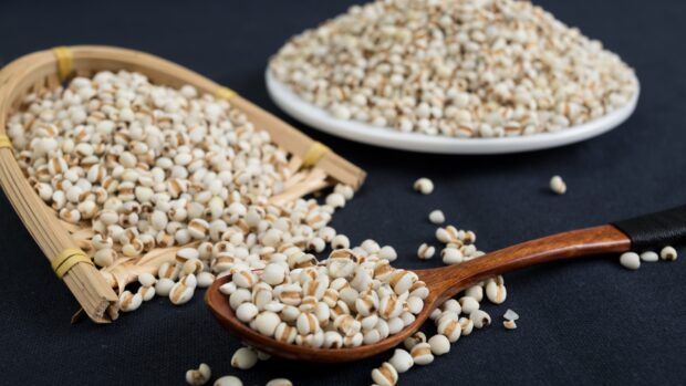 Close up of grains in a wooden spoon and basket on a dark surface