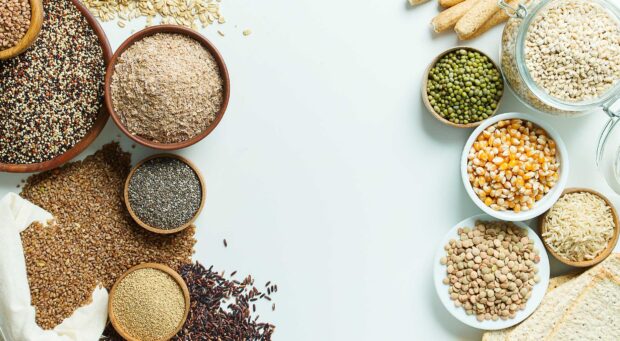 Various grains in wooden bowls displayed on a white table with scattered grains around