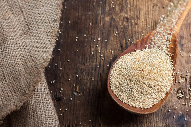A wooden spoon filled with quinoa grains on a rustic wooden surface with a burlap cloth nearby