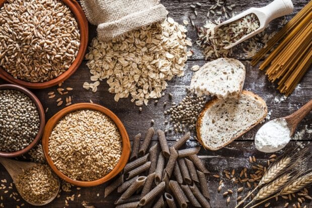 Various grains and seeds in bowls and on a wooden surface with bread and pasta displayed