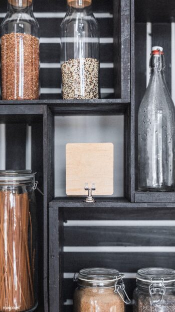 Various grains stored in glass jars on a dark wooden shelf in a kitchen setting