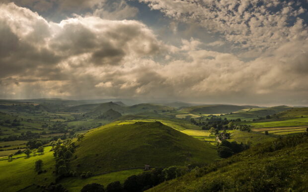 Scenic view of lush grassland hills under dramatic cloudy sky