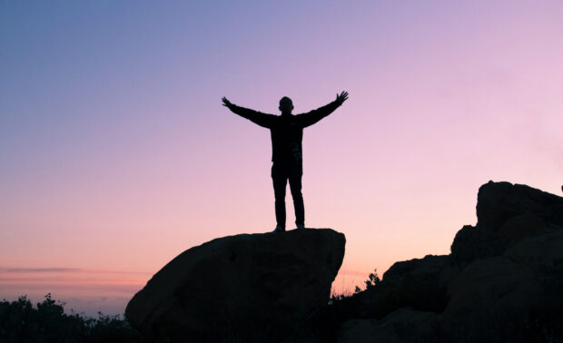Silhouette of person expressing gratitude standing on rock at sunset