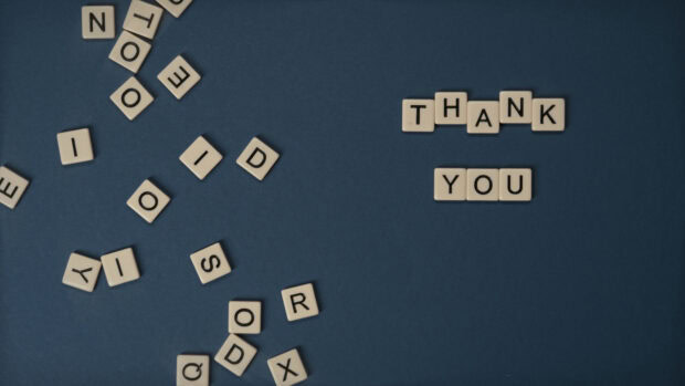 Thank you letters spelled out among scattered alphabet tiles on a blue surface expressing gratitude